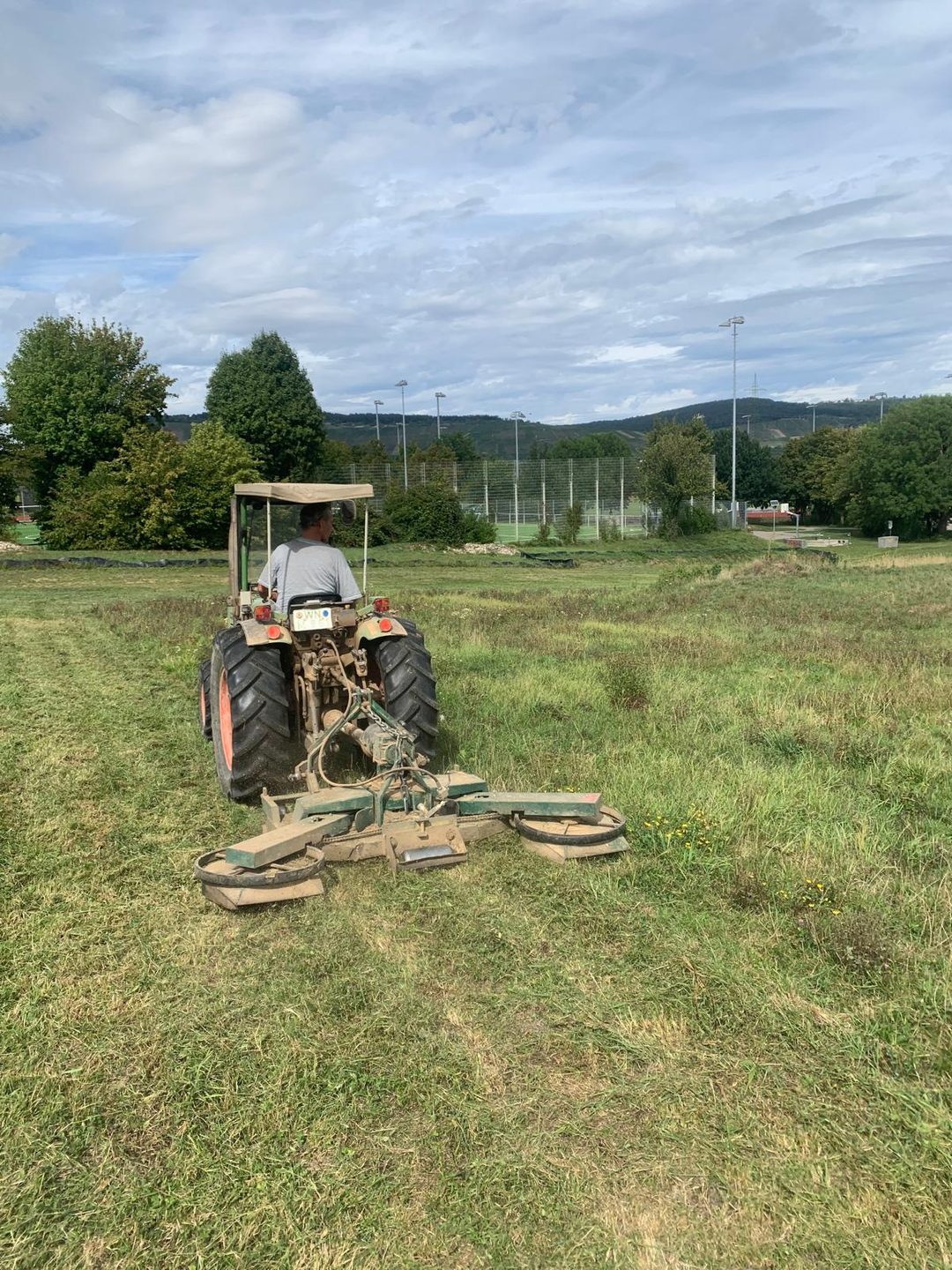 Traktor mit Maehwerk am Sportgelaende
